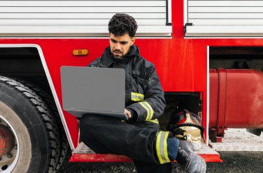 Hispanic fireman using laptop near fire engine